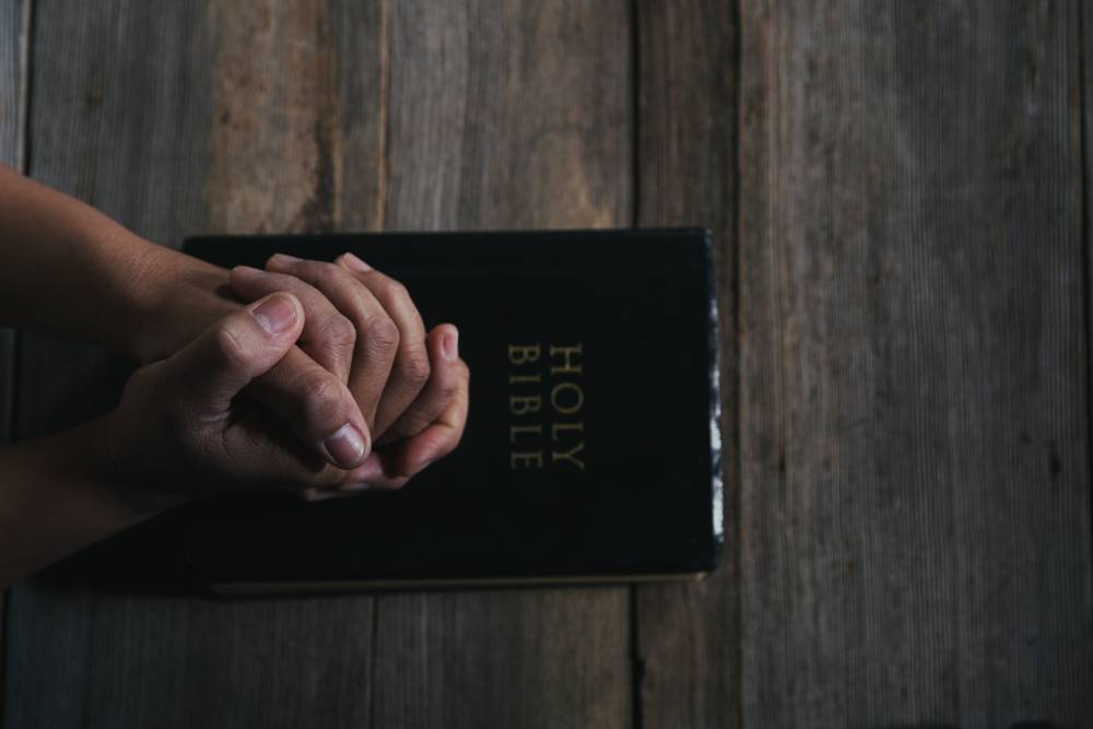 Lost In Translation Ministry Our Videos Hands folded in prayer on a Holy Bible in church concept for faith, spirituality and religion, woman praying on holy bible in the morning. woman hand with Bible praying.
